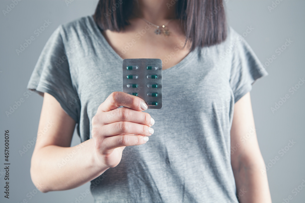 young girl holding pills on gray background