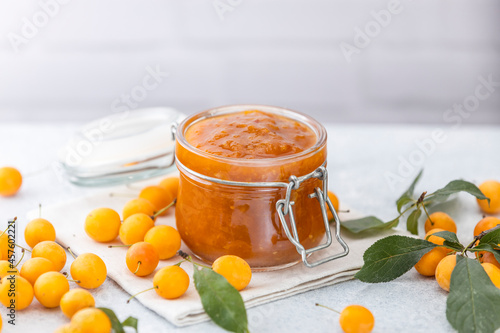 Homemade DIY natural canned yellow cherry plum sauce chutney with chilli or tkemali in glass jar standing on white table photo