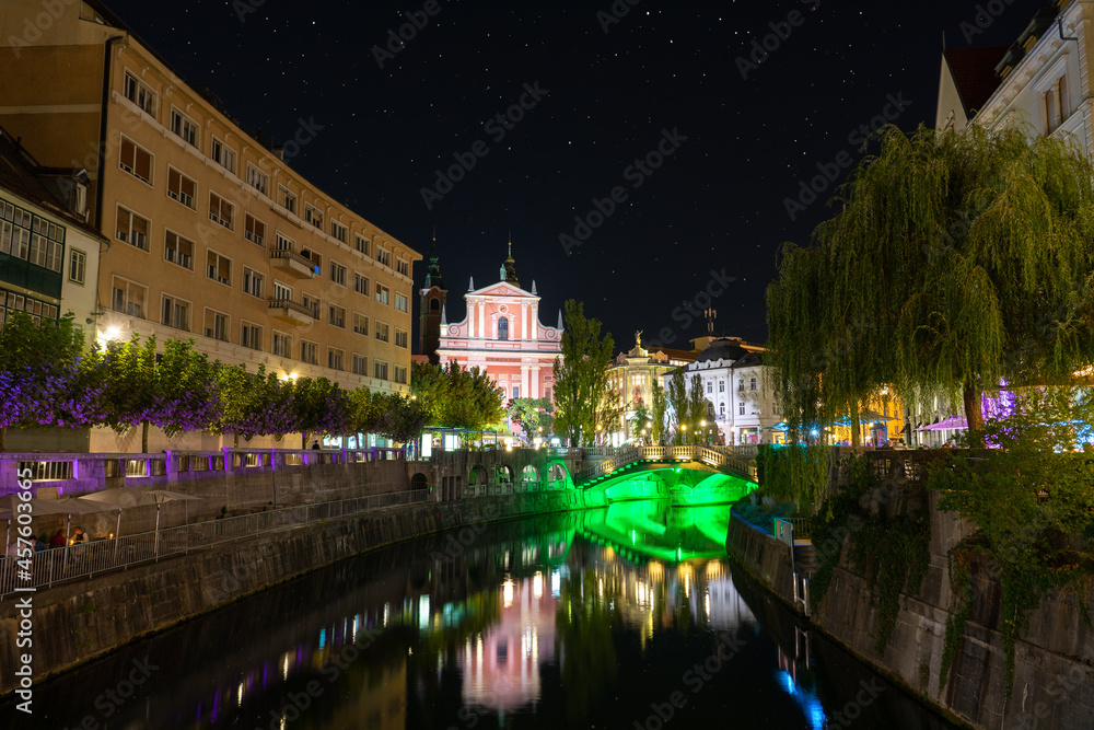 Preseren Square with Tromostovje bridge on Ljubljanica river at night with city lights in Slovenia Ljubjana with Cerkev Marijinega oznanjenja church