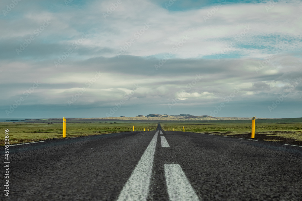 Amazing view of the asphalt road in iceland, leading towards mountains. Leading lines towards lonely mountains in solitude and thick clouds above. Amazing view of the asphalt road in iceland, leading towards mountains. Leading lines towards lonely mountains in solitude and thick clouds above.