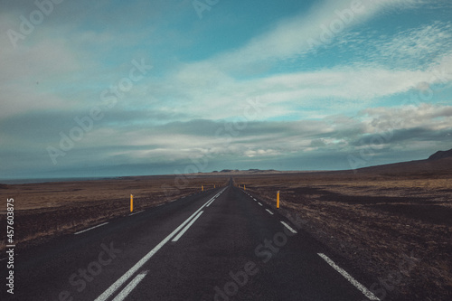 Amazing view of the asphalt road in iceland, leading towards mountains. Leading lines towards lonely mountains in solitude and thick clouds above. © Anze