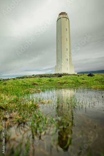 Panoramic view of Malarrif lighthouse on the east of iceland on a cloudy day. Tall Lighthouse in iceland in grey color and thick clouds above and reflection below. photo