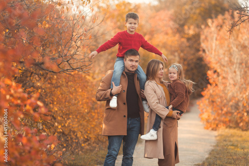 Happy family walking in the fall park. Portrait of a caucasian mother and father holding their children in beautiful outfits on a sunny autumn day in forest. Family lifestyle concept.