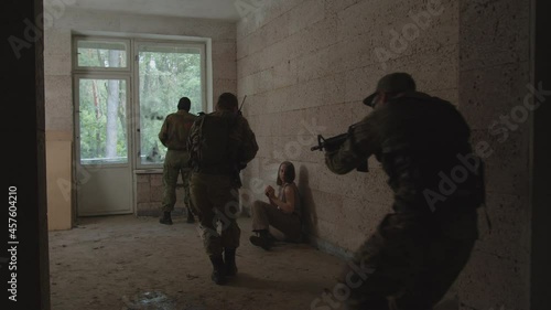 Anti-terrorist soldier eliminating terrorist in balaclava by knife while special forces squad entering room, covering area. Specialist providing psychological assistance to female hostage