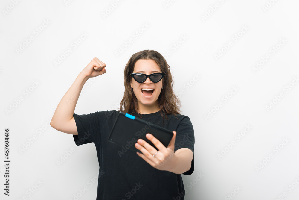 Yes, I have won. Young woman is making the winner gesture while holding a tablet over white background.