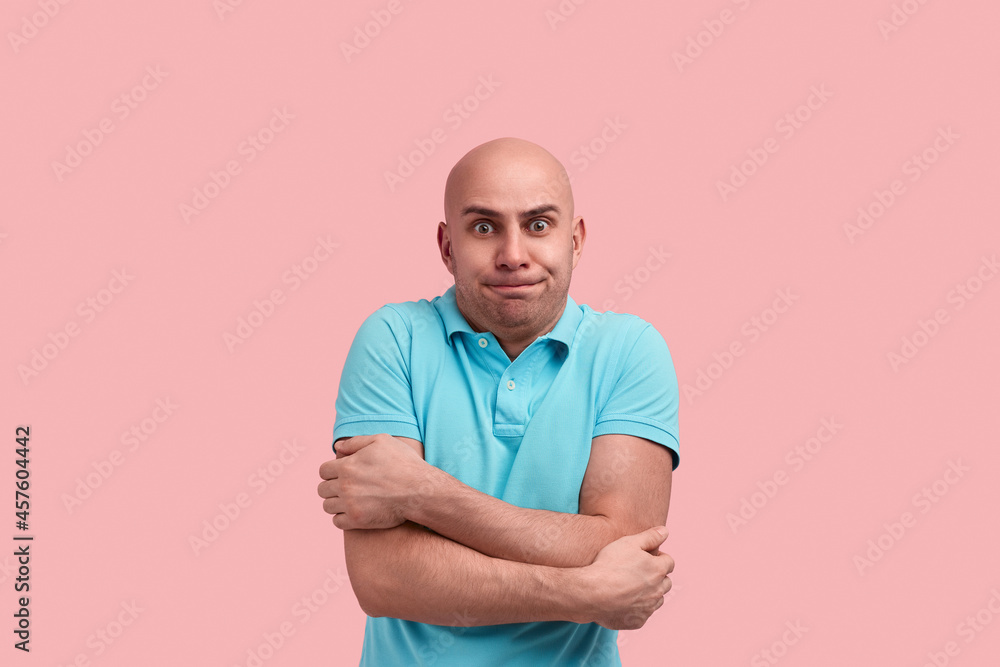 Im trembles. Scared bald homosexual man with bristle feels cold, hugs himself to warm up, clatter with teeth, gay friendly, wears blue polo shirt, poses over pink background. Im trembles. Scared bald homosexual man with bristle feels cold, hugs himself to warm up, clatter with teeth, gay friendly, wears blue polo shirt, poses over pink background.