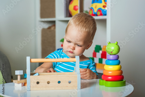 Handsome toddler plays with wooden toys in kindergarten or in children s room close-up and copy space...