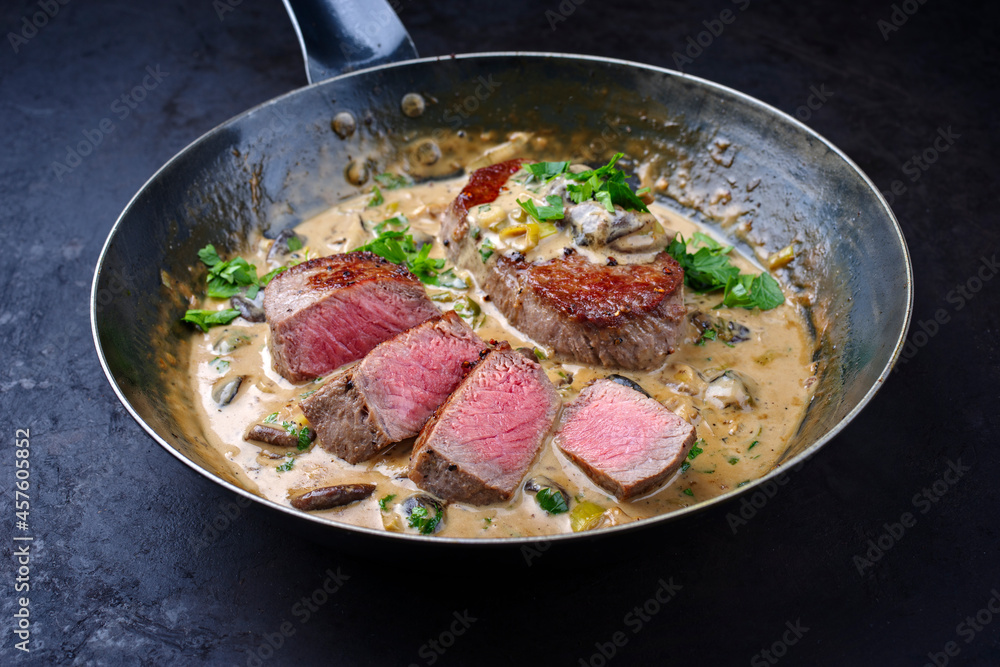 Traditional barbecue dry aged angus roast beef steak natural with mushrooms and onions in cream sauce served as close-up in a classic skillet Traditional barbecue dry aged angus roast beef steak natural with mushrooms and onions in cream sauce served as close-up in a classic skillet