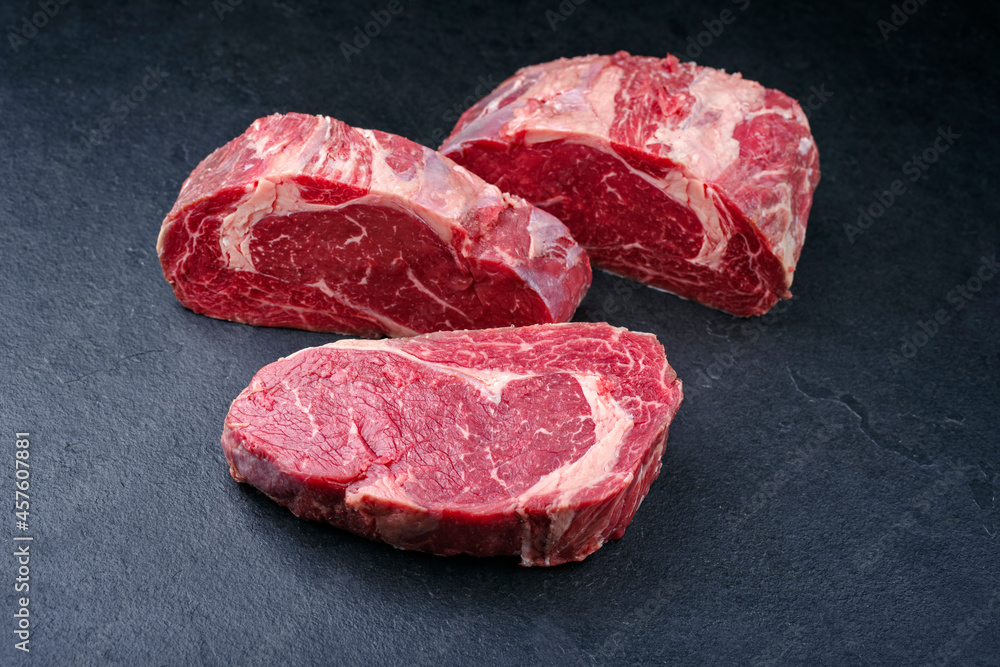 Raw dry aged wagyu rib-eye beef steaks offered as close-up on a black board with copy space