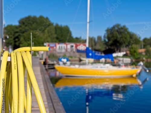 Yellow water hose and yellow sailboat at jetty in Blankaholm guest harbour, Sweden.