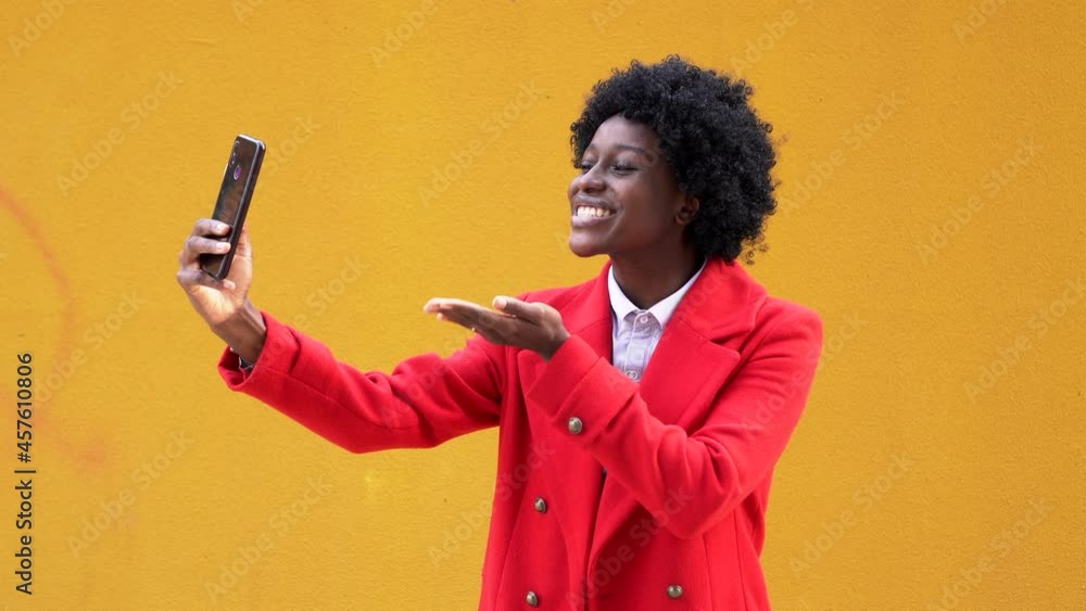 Stylish afro woman blowing an air kiss during a video call with her mobile phone on the street. Technology and communication concept. Stylish afro woman blowing an air kiss during a video call with her mobile phone on the street. Technology and communication concept.