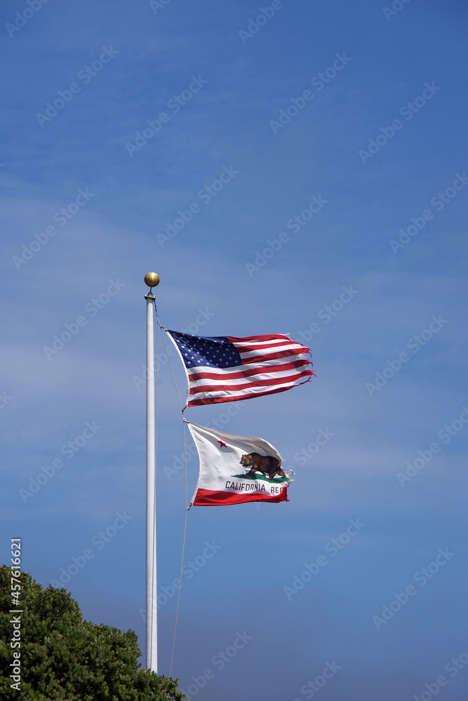The US and California flags waving high in the wind under blue sky
