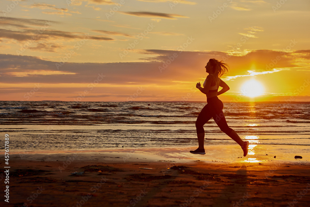 Woman runs on sand near coast during sunset.