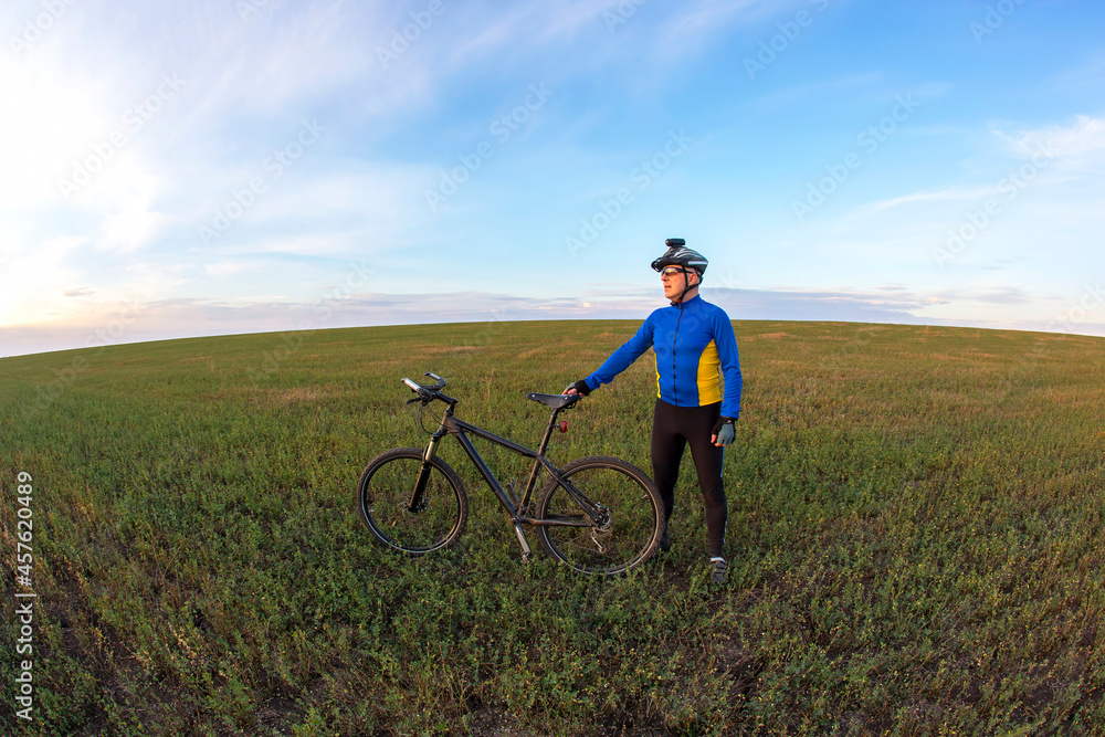 cyclist with a bicycle is resting on a green field against a blue sky. sports and recreation in nature cyclist with a bicycle is resting on a green field against a blue sky. sports and recreation in nature