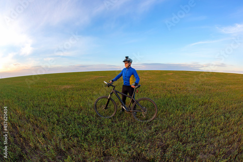 cyclist with a bicycle is resting on a green field against a blue sky. sports and recreation in nature © photosaint