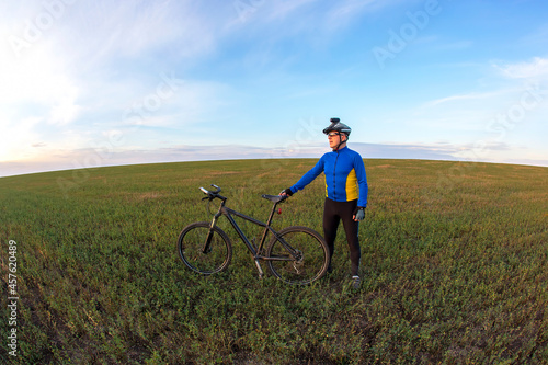 cyclist with a bicycle is resting on a green field against a blue sky. sports and recreation in nature