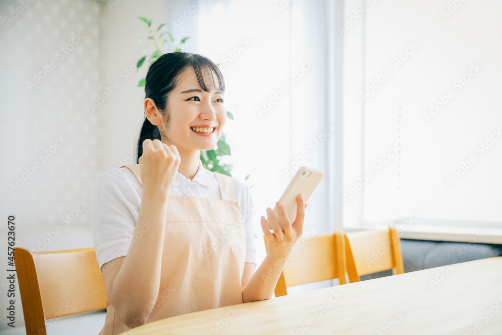 スマホを使うエプロン姿の女性(ガッツポーズ)
スマホを使うエプロン姿の女性(ガッツポーズ)