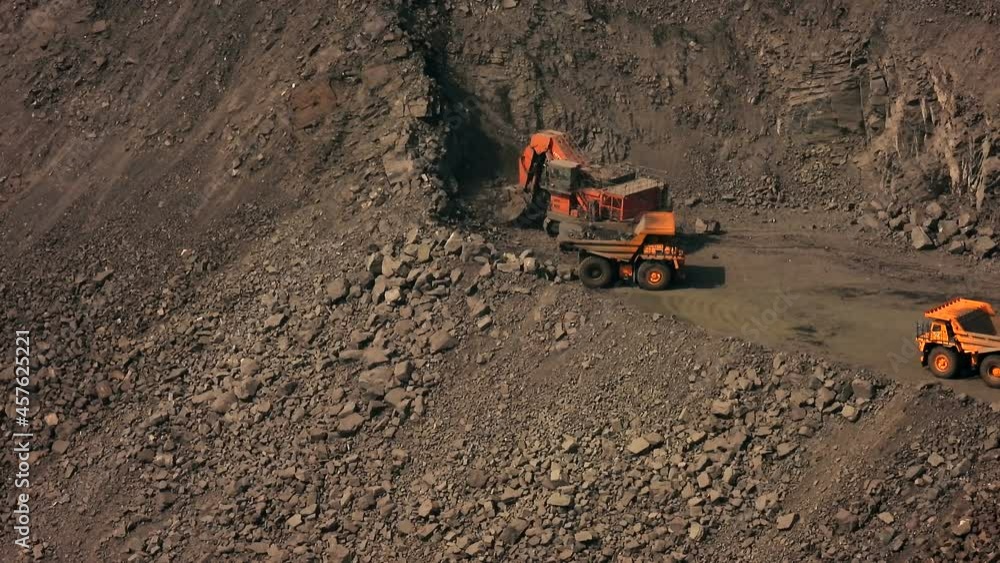 Yellow excavator shovels ore with a bucket in a quarry and pours it
