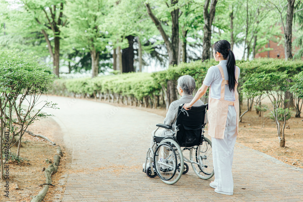 車椅子に乗った高齢者女性と女性スタッフ（後ろ姿・全身）
