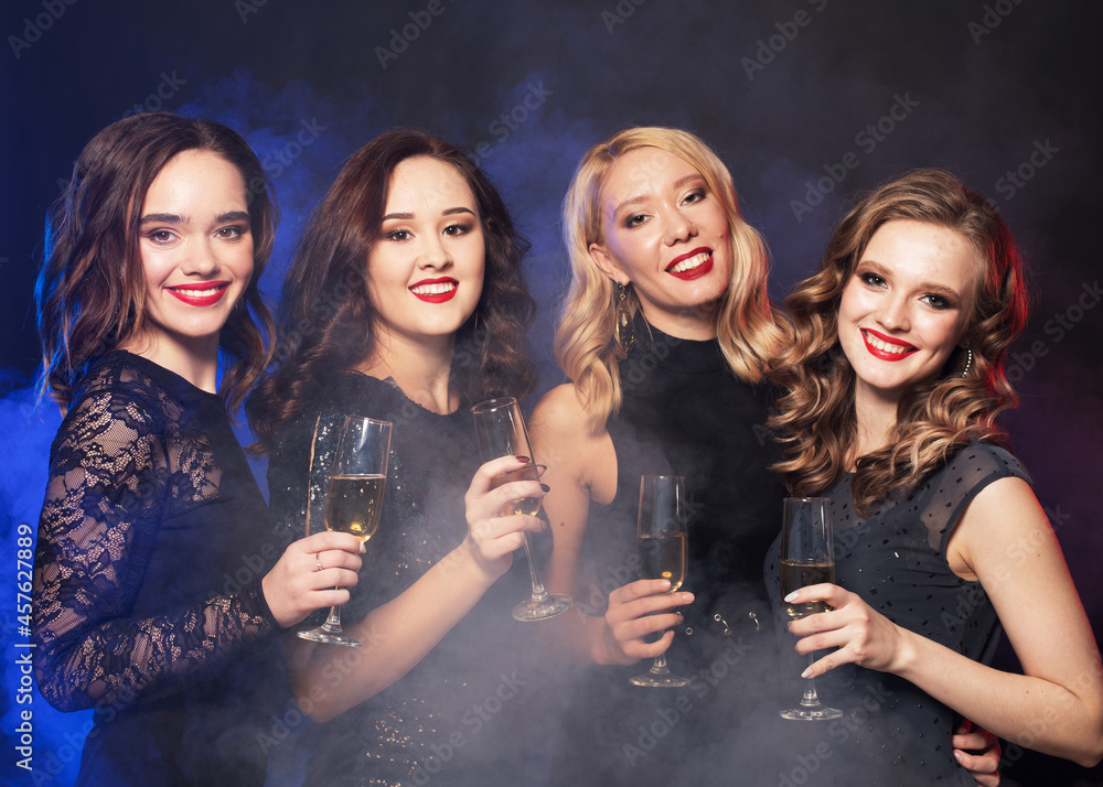 party and people concept - young women clinking flutes with sparkling wine over dark background. party and people concept - young women clinking flutes with sparkling wine over dark background.