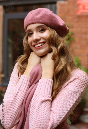 Outdoor portrait of young beautiful woman with long wavy hair, wearing pink beret and scarf