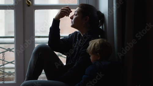 Preoccupied mother sitting by window with toddler. anxious parent photo
