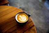 Cup of cappuccino with latte art on wooden background. Beautiful foam, wooden desk and bricks wall.