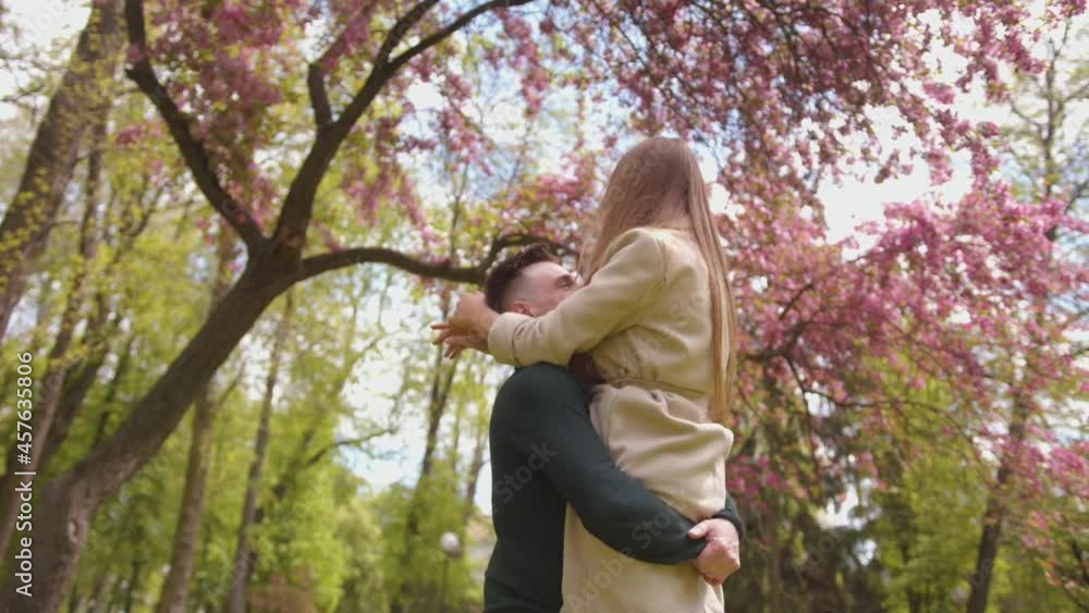 A young man is circling in his arms a charming young girl under a tree with lilac flowers. Love and happiness concept A young man is circling in his arms a charming young girl under a tree with lilac flowers. Love and happiness concept