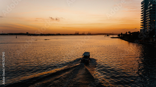 Bote navegando por la bahía en amanecer con cielo naranja y amarillo con edificios, grúas y Sociedad Portuaria de fondo. Cartagena de Indias, Colombia photo