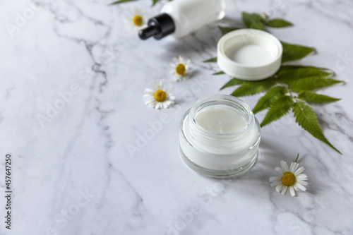Natural cosmetic products. Daily hygiene and female healthy skincare. Cosmetic cream and skin care serum with cammomile flofers on marble countertop. SPA natural organic beauty product. Copy space.