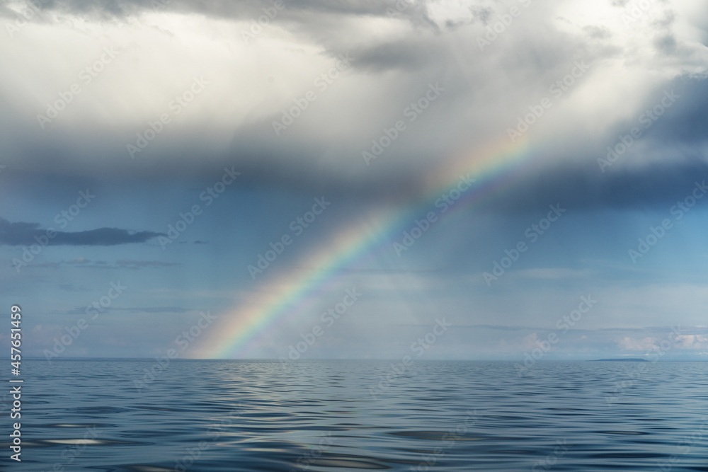 Multicolored rainbow over the endless blue sea and cloudy sky. Wonderful landscape. After the rain.