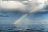 Multicolored rainbow over the endless blue sea and cloudy sky. Wonderful landscape. After the rain.