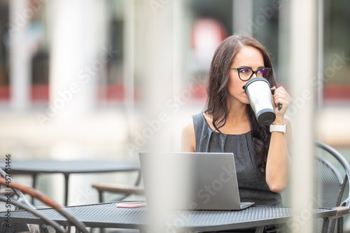 Beautiful brunette sipping coffee from sustainable coffee mug outdoors while she works on the laptop in an offce enviroment photo