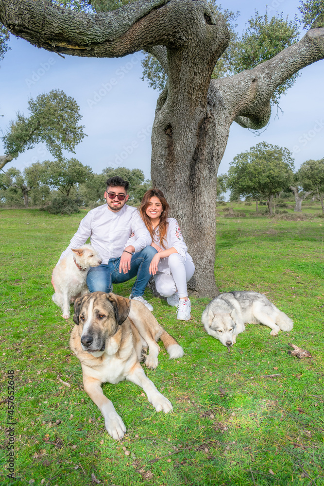 young couple next to an oak tree with three dogs