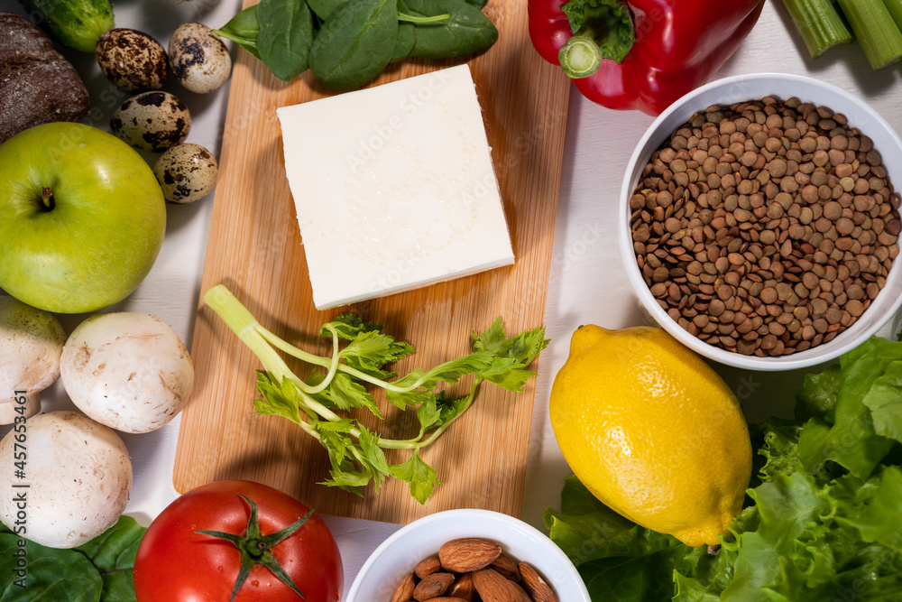 Feta cheese on a wooden cutting board surrounded by other ingredients for a Greek salad. Vegetarian dish. Light food. Close-up, top view. Feta cheese on a wooden cutting board surrounded by other ingredients for a Greek salad. Vegetarian dish. Light food. Close-up, top view.
