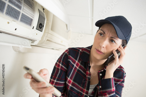 air conditioning engineer holding remote control and talking on smartphone photo