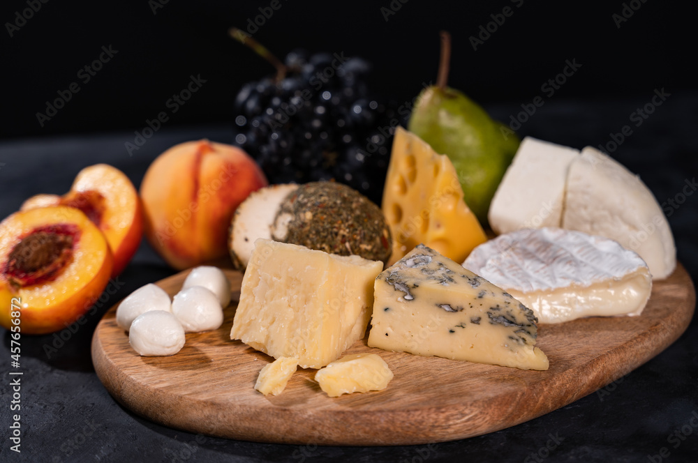 Various kinds of cheese with walnuts and grapes. Wine plate. Close-up, dark background.