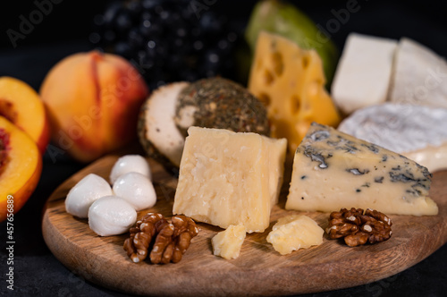 Various types of cheese on a dark background. Nearby are peaches, grapes, nuts. An exquisite delicacy. Close-up.