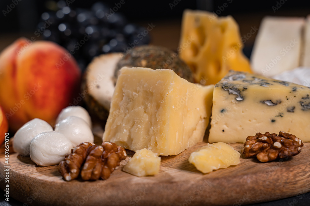Parmesan and walnuts on a wooden board. In the background mozzarella, peaches, grapes. Close-up, dark background.