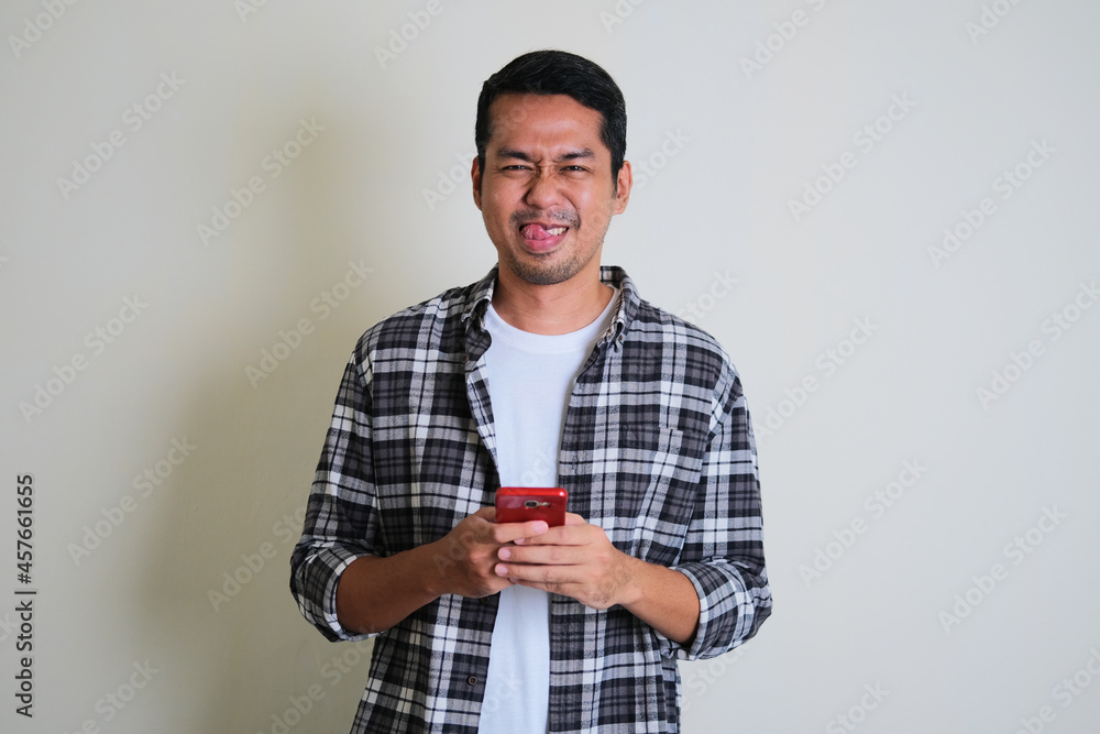 Young Asian man showing silly face expression while texting on his mobile phone Young Asian man showing silly face expression while texting on his mobile phone