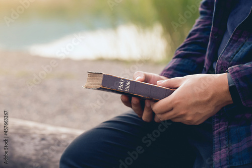 male sitting and holding Bible in his hands with nature background.Sunday readings, Bible