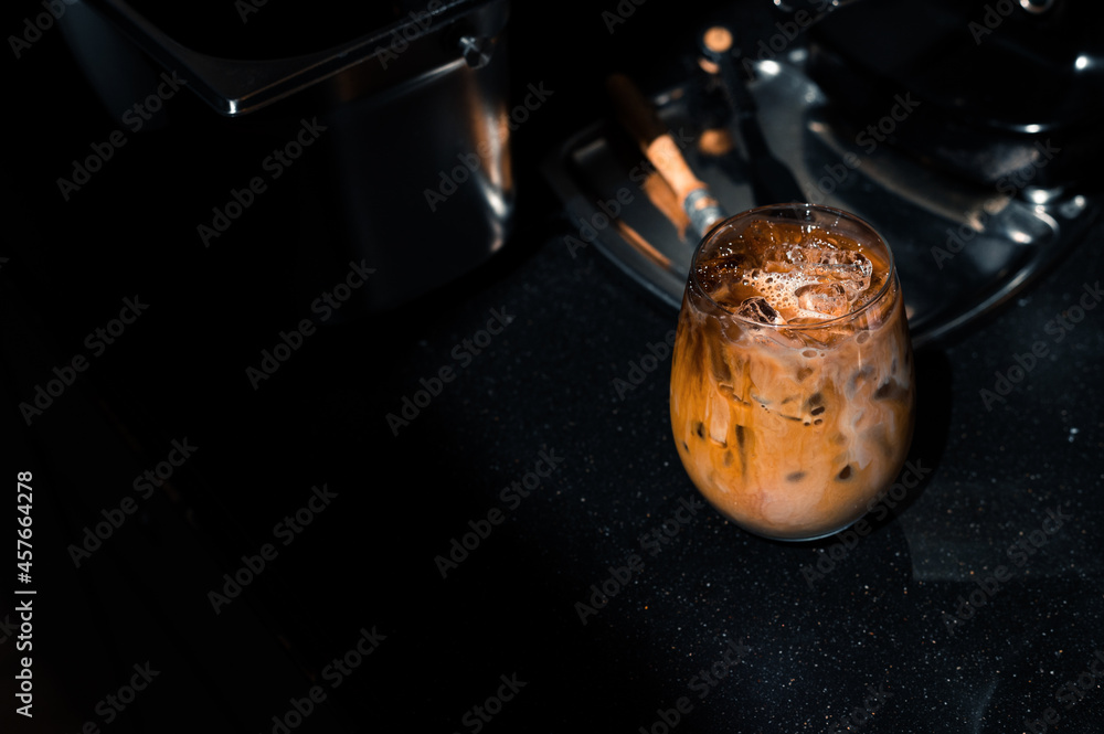 Fototapeta premium iced coffee in iridescent stemless glass served on black table at cafe​