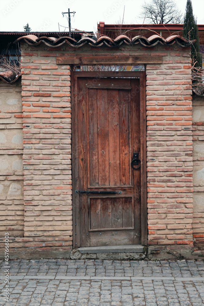 Wooden door with a round metal handle on the brick wall