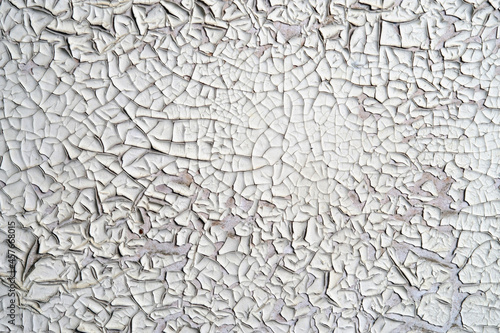 White peeling paint on the wall. Weathered rough painted surface with patterns of cracks