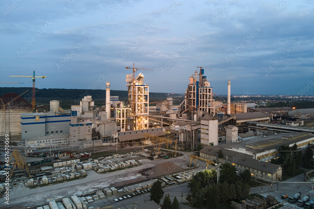Aerial view of cement factory with high concrete plant structure and tower cranes at industrial production area at night. Manufacture and global industry concept.