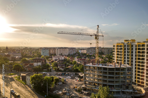 Apartment or office tall building under construction. Brick walls, glass windows, scaffolding and concrete support pillars. Tower crane on bright blue sky copy space background.