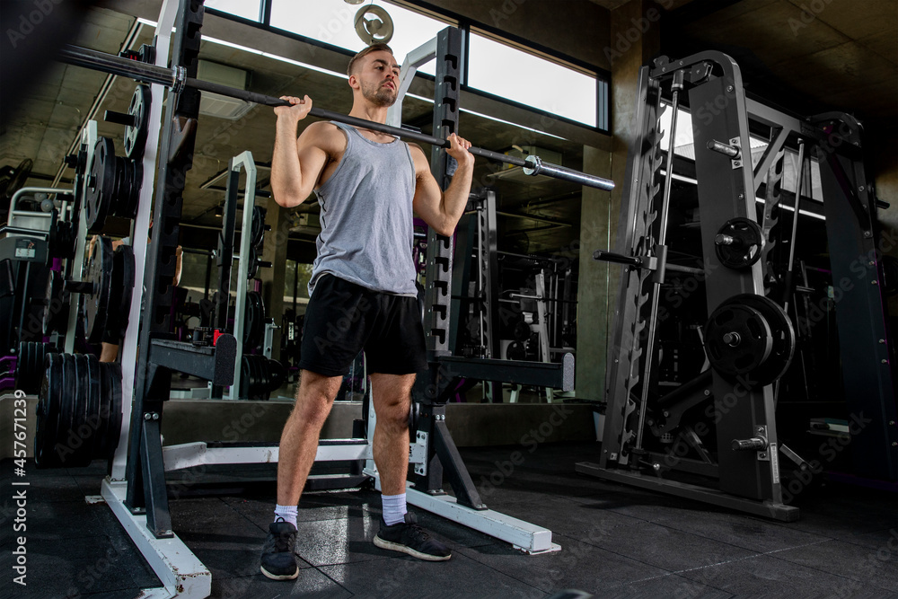Fit young man lifting barbells looking focused, working out in a gym Fit young man lifting barbells looking focused, working out in a gym