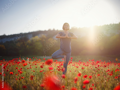 Fototapeta Naklejka Na Ścianę i Meble -  A beautiful woman meditates on a poppy field at sunset. Wellness well-being happiness concept.
