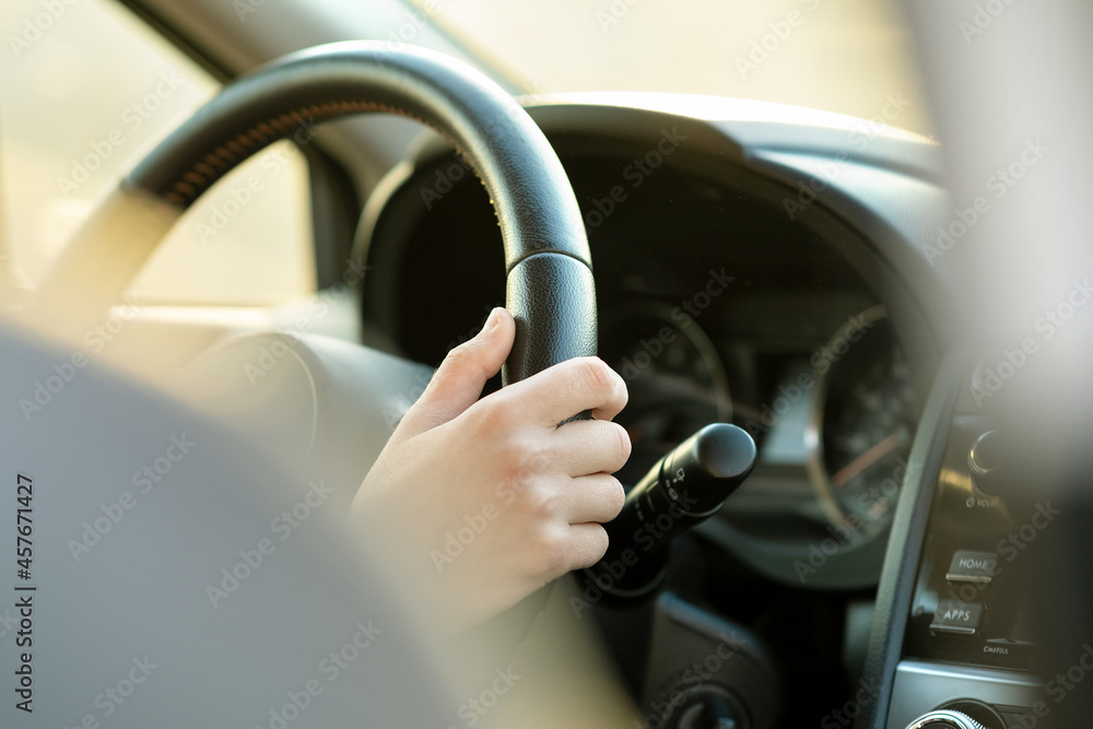 Close up view of woman hands holding steering wheel driving a car on city street on sunny day. Close up view of woman hands holding steering wheel driving a car on city street on sunny day.