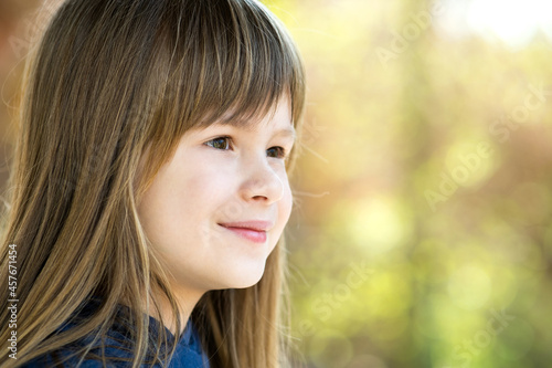Portrait of pretty child girl with gray eyes and long fair hair smiling outdoors on blurred bright background. Cute female kid on warm summer day outside.